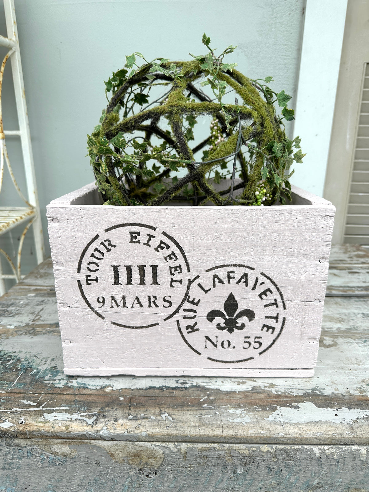 Decorative wooden box with French text and a spherical green plant on a wooden surface.
