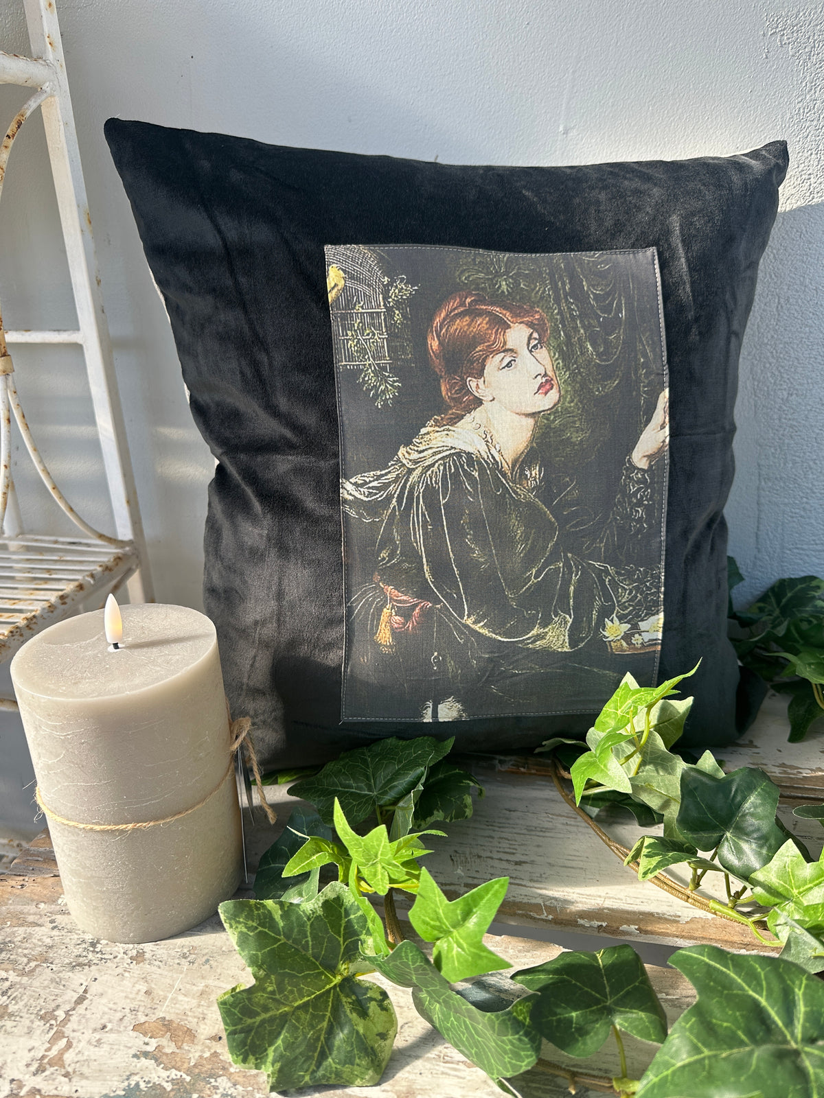 Black pillow with a printed design of a woman leaning against a wall, placed on a ledge with greenery. Velvet Cushion Midnight Veronica II The Villa Collection