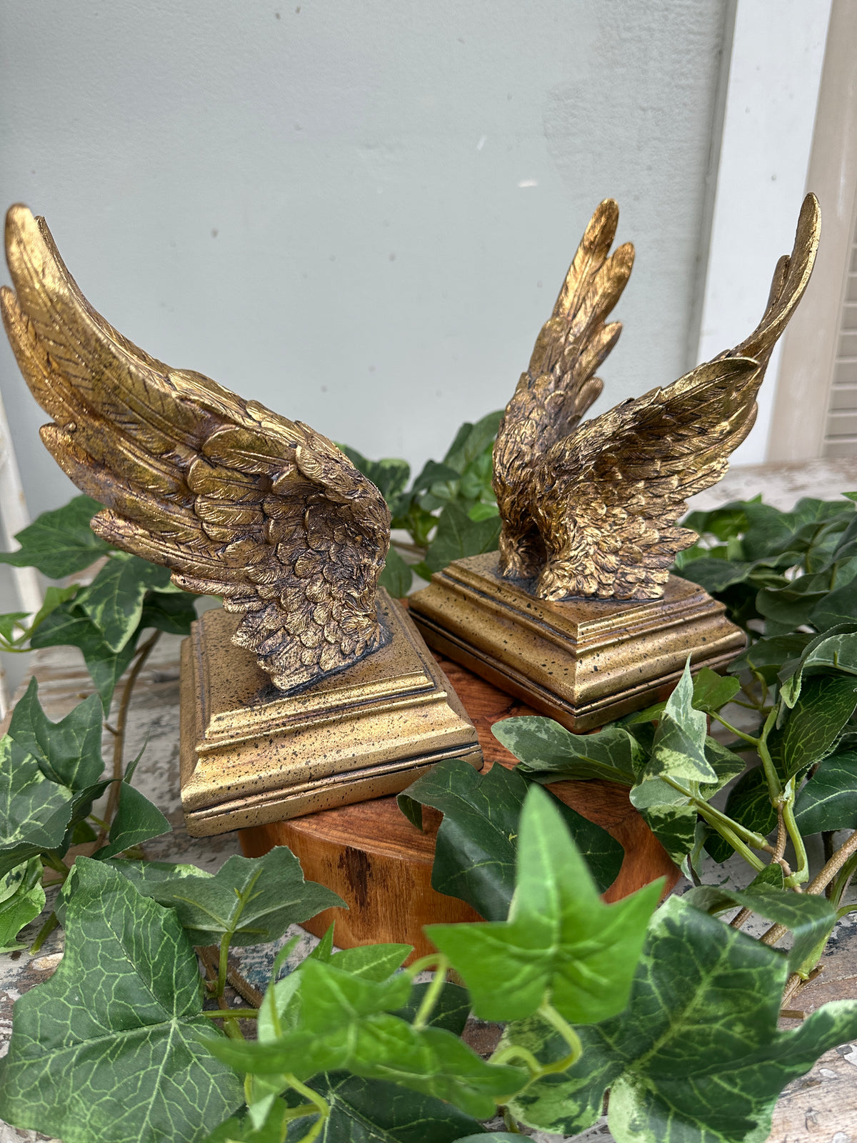Decorative wreath with gold angel wings and framed pictures on a wall.