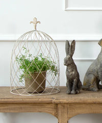 Decorative wire cloche with a plant on a wooden surface, accompanied by stone rabbit sculptures. Wire Cloche Dome medium by French Country Collections