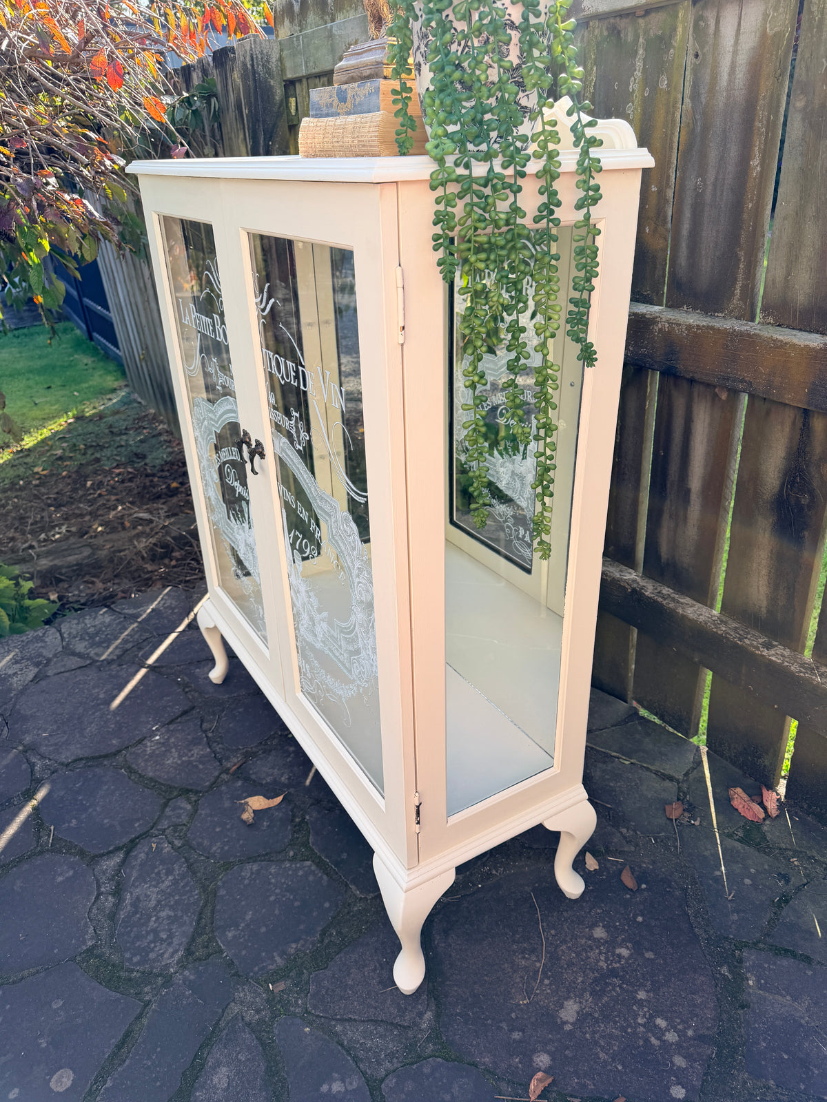 Cabinet with glass doors featuring embossed designs and text. Limestone Cream & White mirrored Display Cabinet with glass shelves