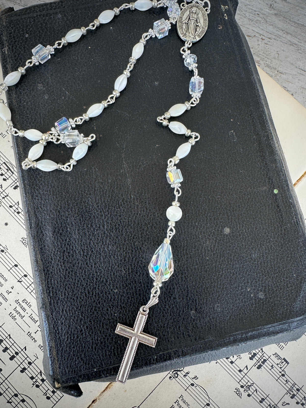 Silver rosary with clear beads on a black book with music notes. Decor prayer beads Clear, white and Silver