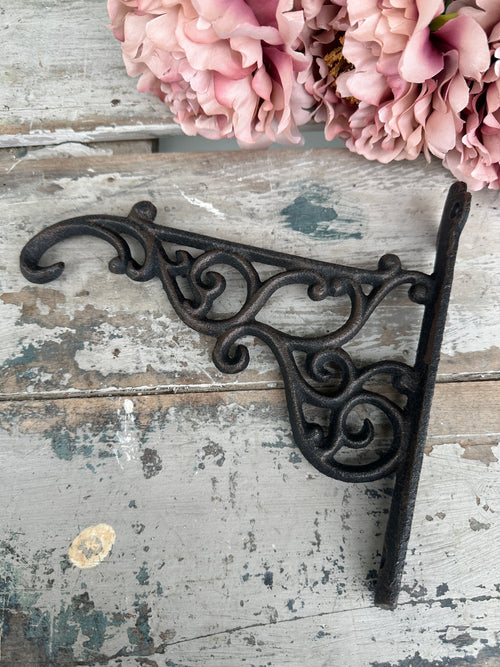 Decorative metal bracket on a rustic wooden surface with pink flowers. Shelf or Fancy Plant Bracket Cast Iron