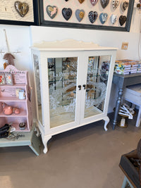 Cabinet with glass doors featuring embossed designs and text. Limestone Cream & White mirrored Display Cabinet with glass shelves