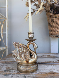 A decorative swan-shaped candle holder in a distressed gold finish,