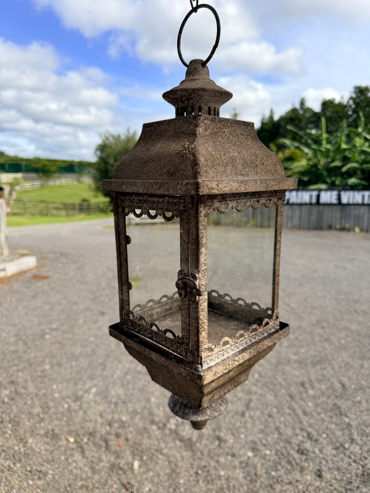 Decorative metal lantern on a road with a blue sky and trees in the background