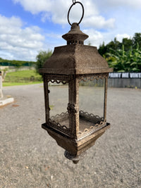 Decorative metal lantern on a road with a blue sky and trees in the background