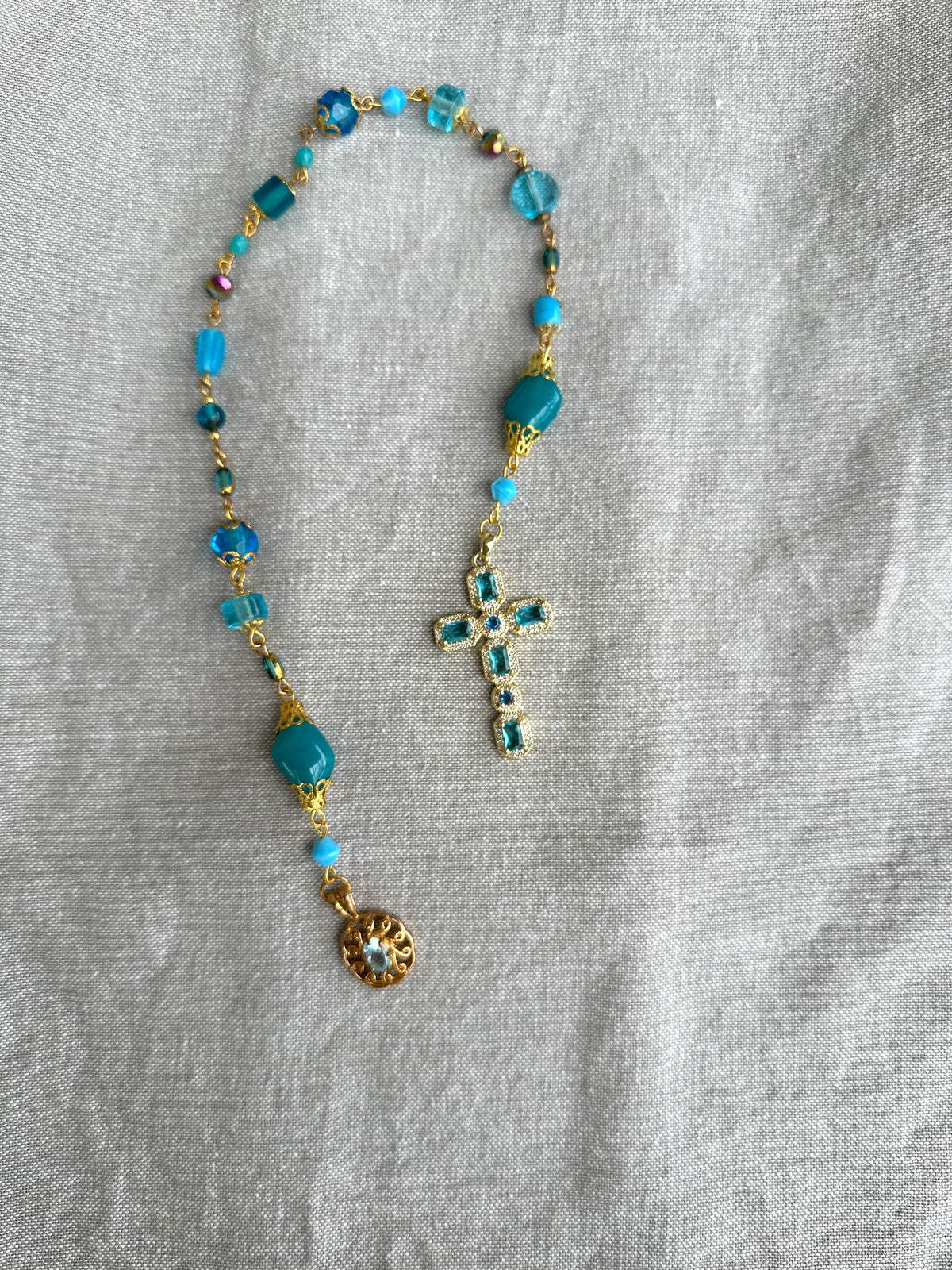Rosary with blue beads and a cross on a gray fabric background