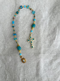 Rosary with blue beads and a cross on a gray fabric background