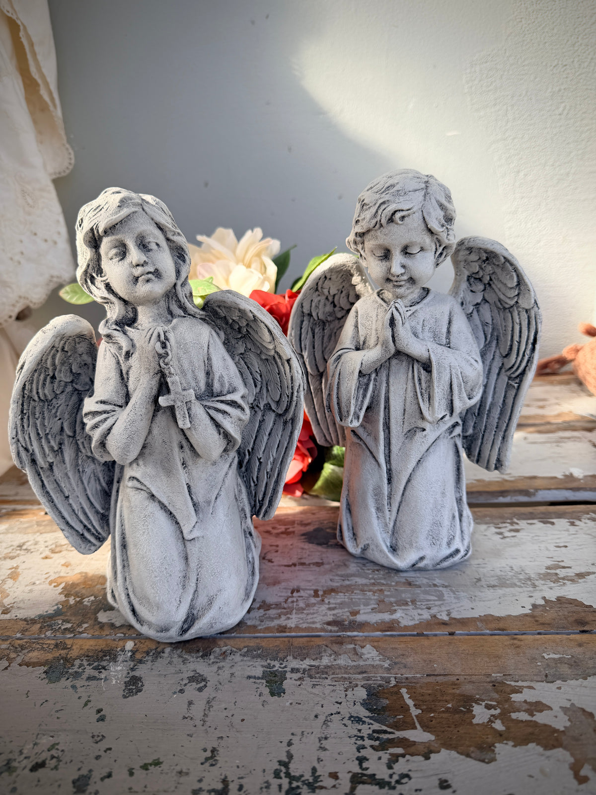A weathered gray stone angel statue kneeling and holding a rosary. Blessed Statue painted