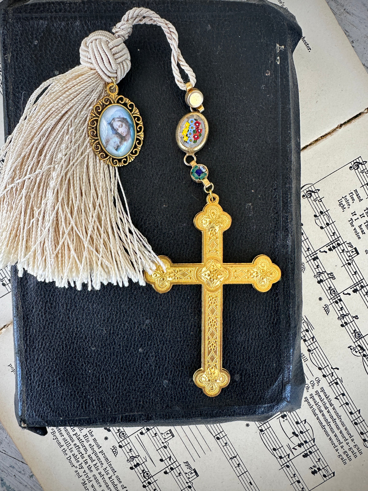 Decorative gold cross with tassel on a black book with sheet music in the background. Decor prayer beads with and Tassel