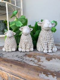 Three textured stone sheep figurines in cream and light gray tones, arranged from smallest to largest. Concrete whitewash look sheep sitting