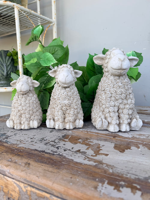 Three textured stone sheep figurines in cream and light gray tones, arranged from smallest to largest. Concrete whitewash look sheep sitting