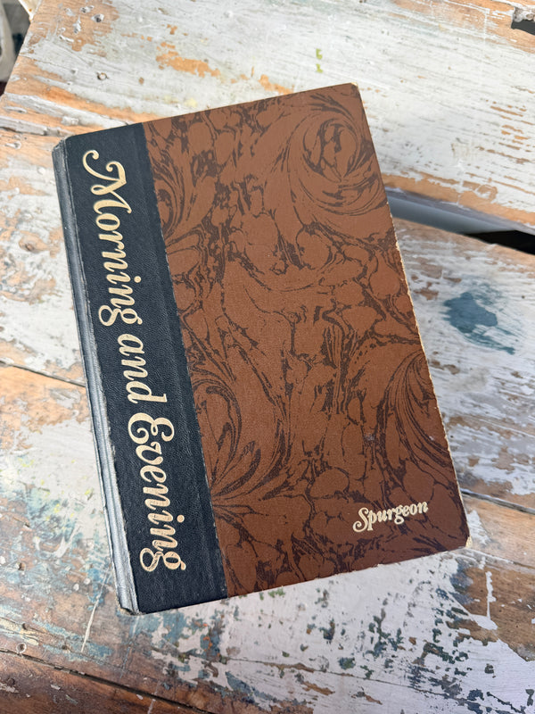 Brown book with decorative cover and 'Morning and Evening' text on a rustic wooden surface