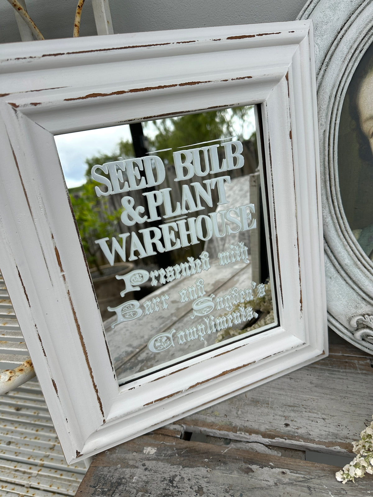 Decorative mirror with text in a rustic white frame on a wooden surface.