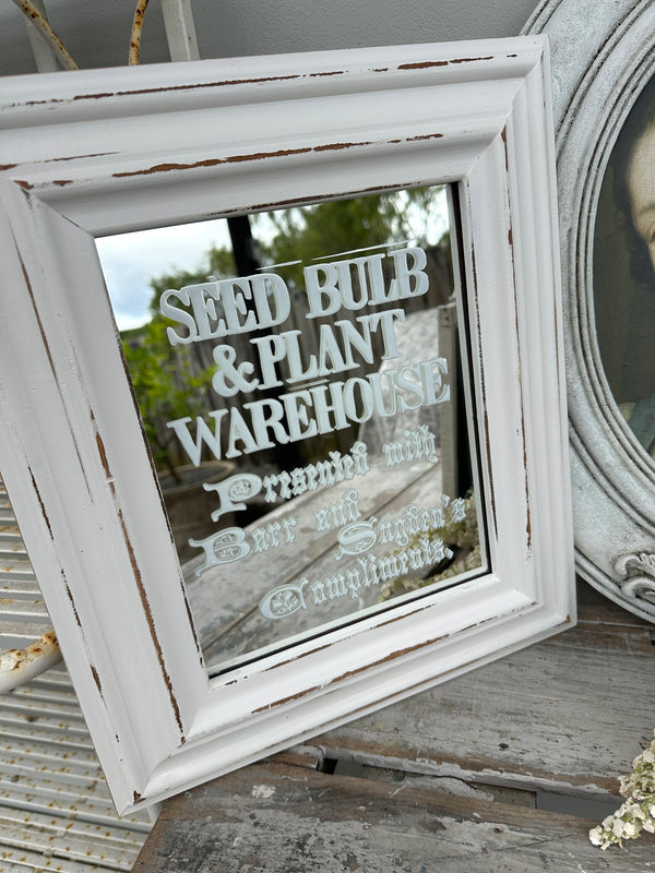 Decorative mirror with text in a rustic white frame on a wooden surface.
