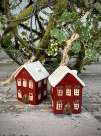 Two red ceramic houses with white roofs on a rustic surface with greenery in the background. French Country Hanging Mini House