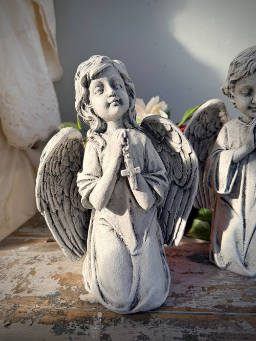 A weathered gray stone angel statue kneeling and holding a rosary. Blessed Statue painted