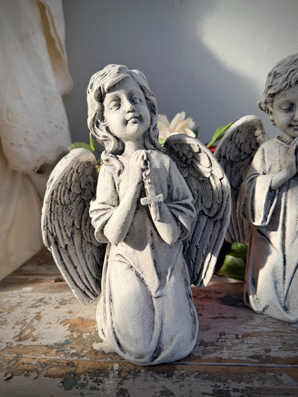 A weathered gray stone angel statue kneeling and holding a rosary. Blessed Statue painted
