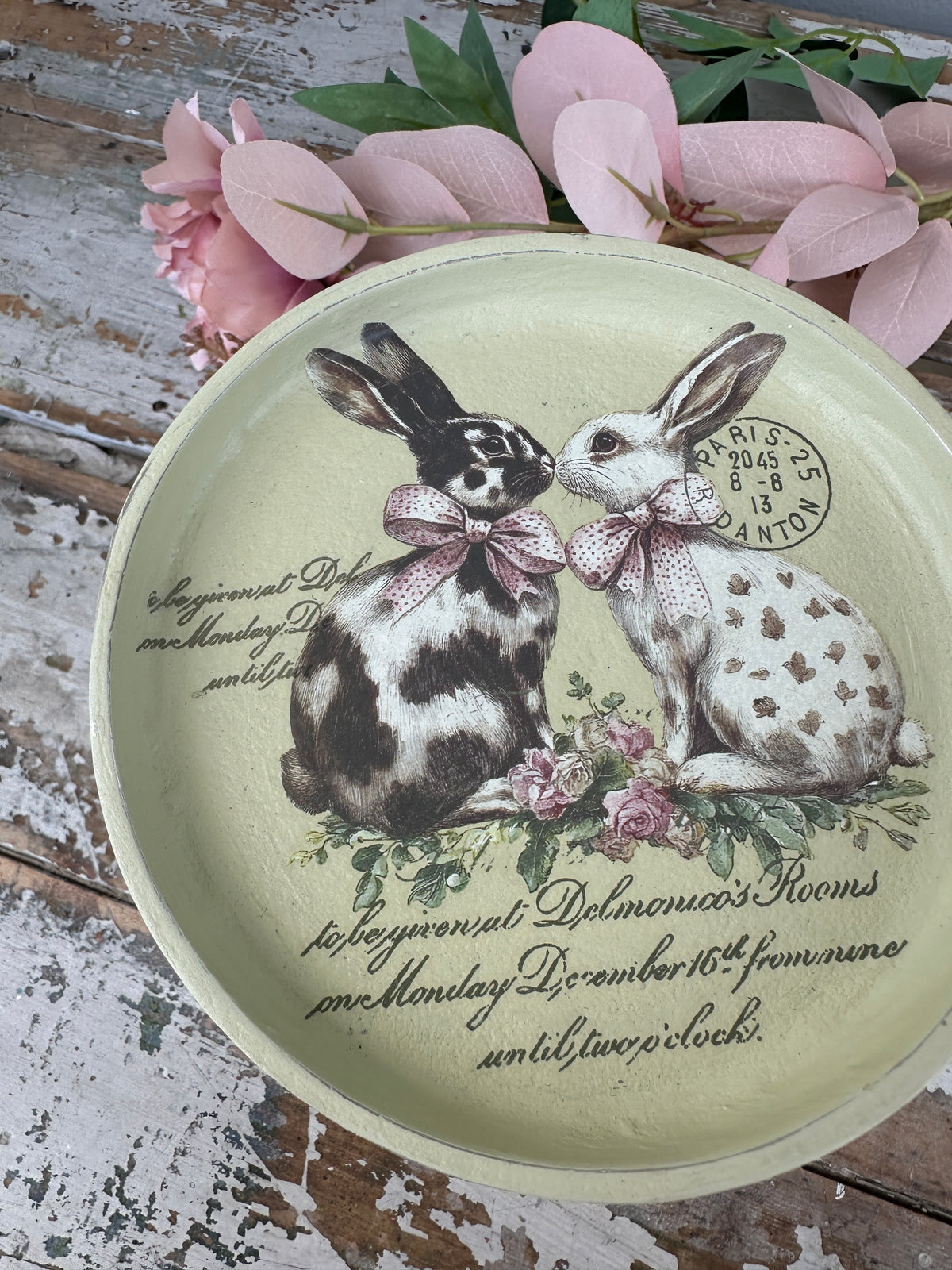 Decorative plate with rabbits and floral design on a rustic wooden surface.
