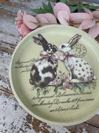 Decorative plate with rabbits and floral design on a rustic wooden surface.