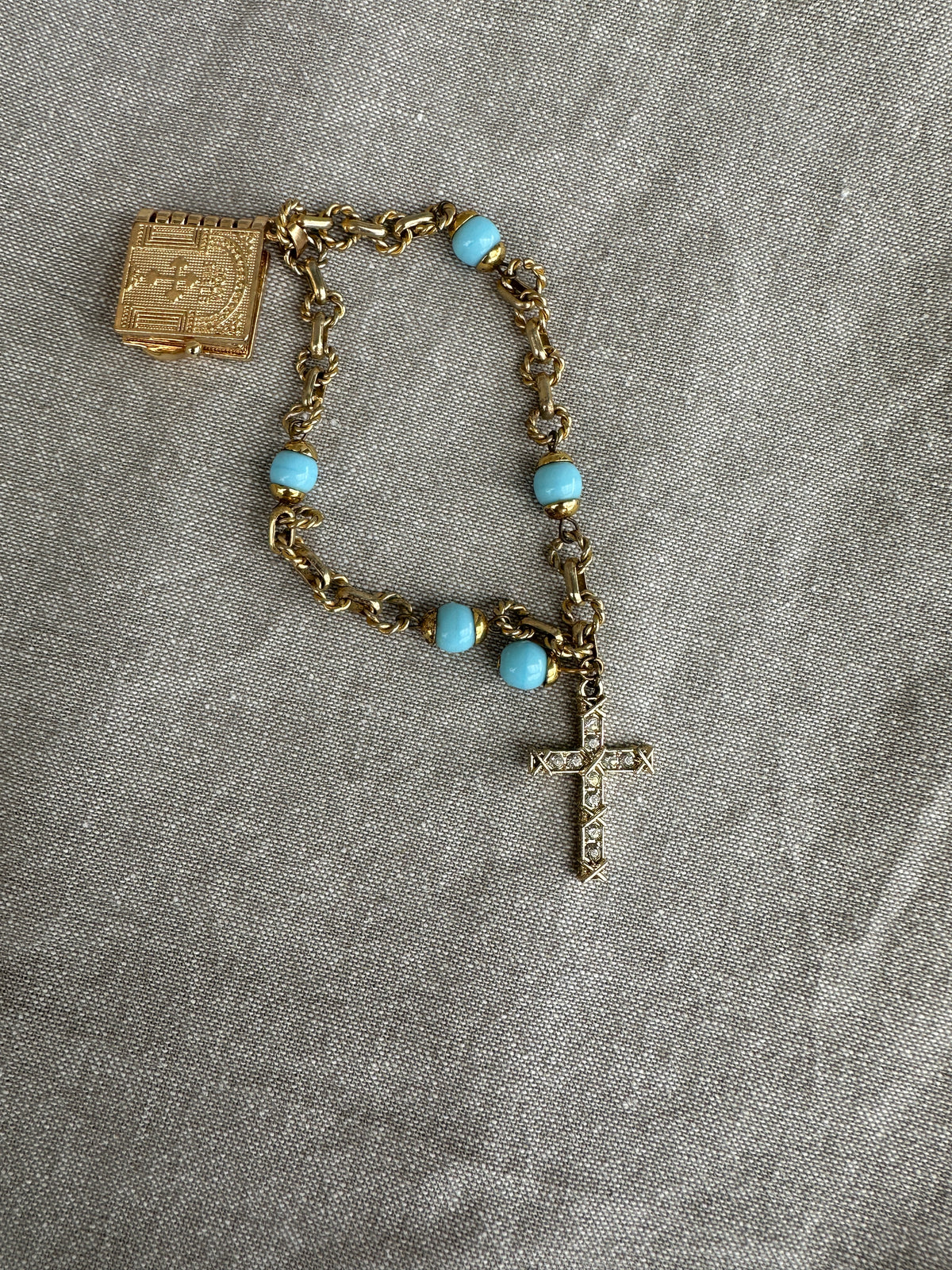 Vintage rosary bracelet with turquoise beads and gold chain on a gray fabric background
