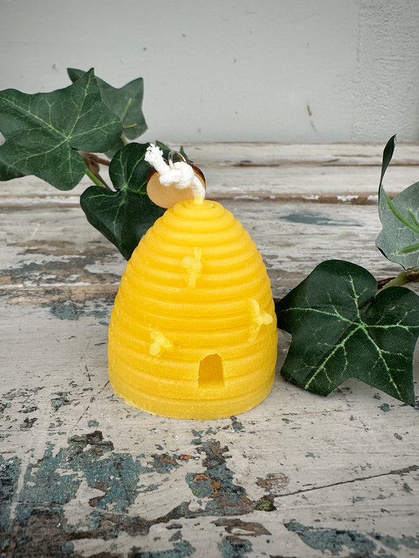 Yellow beehive-shaped candle with a white bee on top, placed on a textured surface with green leaves.