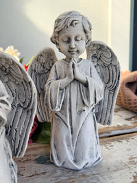 A gray stone-look angel figurine with closed eyes, hands together in prayer, and detailed wings. At Peace Statue painted.