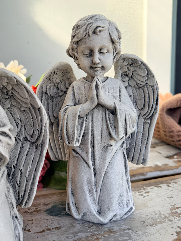 A gray stone-look angel figurine with closed eyes, hands together in prayer, and detailed wings. At Peace Statue painted.