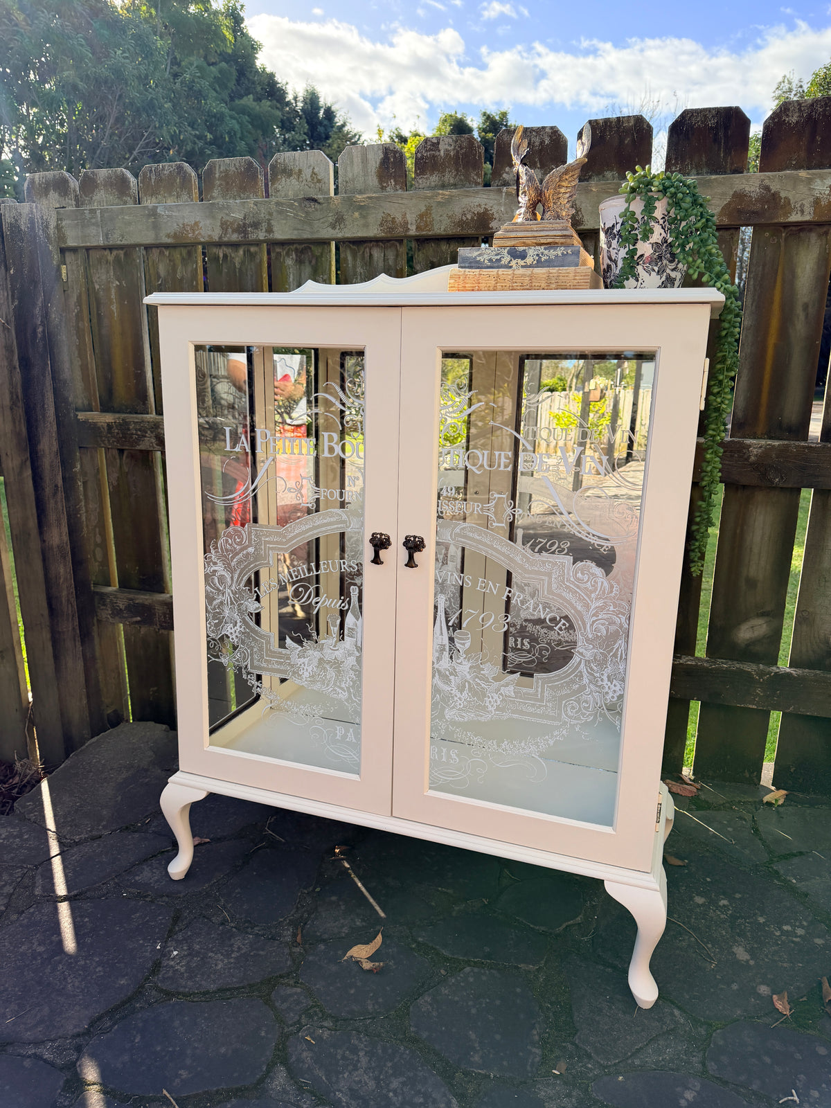 Cabinet with glass doors featuring embossed designs and text. Limestone Cream & White mirrored Display Cabinet with glass shelves