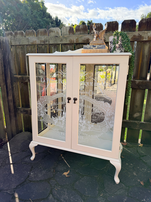 Cabinet with glass doors featuring embossed designs and text. Limestone Cream & White mirrored Display Cabinet with glass shelves