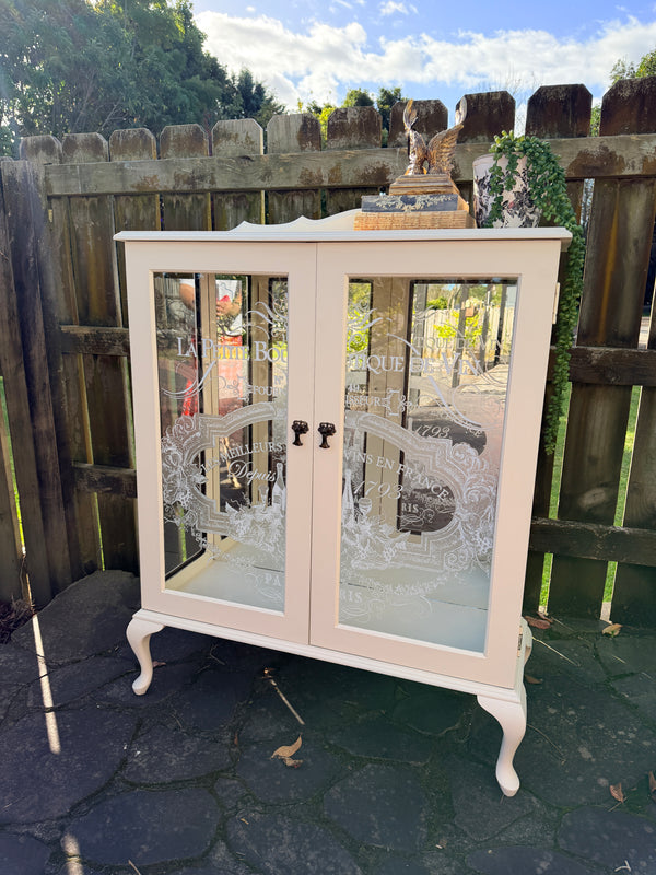 Cabinet with glass doors featuring embossed designs and text. Limestone Cream & White mirrored Display Cabinet with glass shelves
