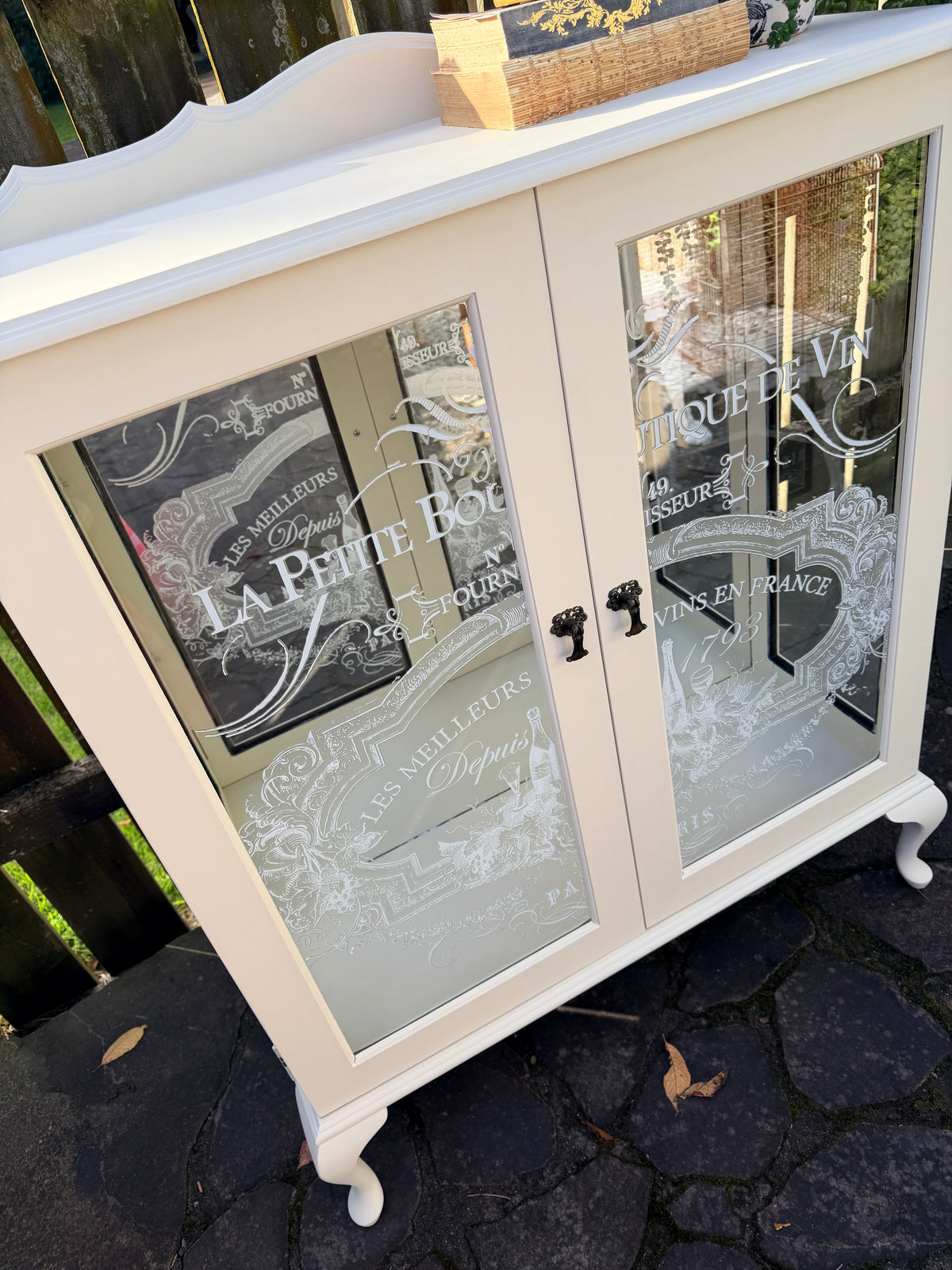 Cabinet with glass doors featuring embossed designs and text. Limestone Cream & White mirrored Display Cabinet with glass shelves