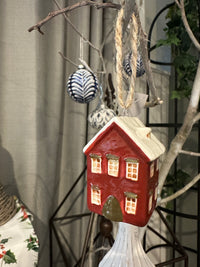 Decorative house-shaped birdhouse on a surface with branches and plants in the background French Country Hanging Mini House