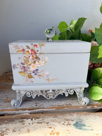 Decorative box with floral and bird design on a stand with greenery in the background. Filigree Blue Lidded Box