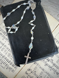 Rosary on a black book with sheet music underneath. Decor prayer beads Clear, white and Silver