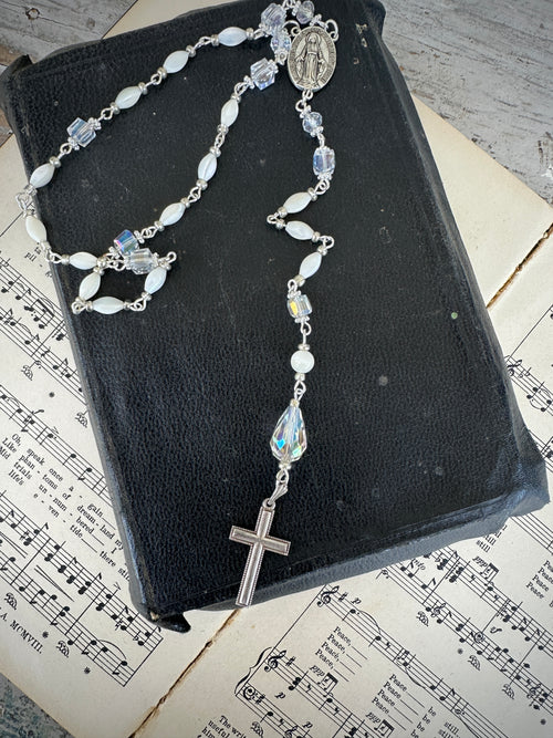 Rosary on a black book with sheet music underneath. Decor prayer beads Clear, white and Silver