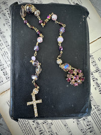 Rosary with colorful beads on a black leather book with music sheet background. Decor prayer beads lilacs w round jewelled end