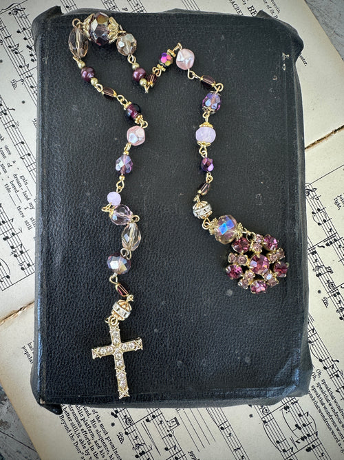 Rosary with colorful beads on a black leather book with music sheet background. Decor prayer beads lilacs w round jewelled end