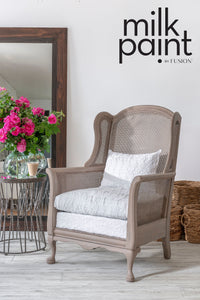 Chair with white cushions in a room with flowers and a mirror, featuring 'milk paint by Fusion' text. Almond Latte Fusion Milk Paint