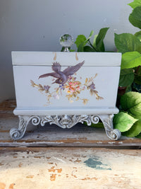 Decorative box with floral and bird design on a stand with greenery in the background. Filigree Blue Lidded Box