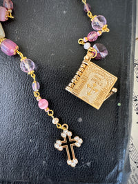Rosary with pink beads and gold cross on a textured surface