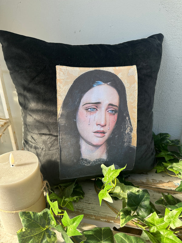 Black pillow with a portrait print of a woman's face on a white surface with greenery. Velvet Cushion Midnight Mary II The Villa Collection