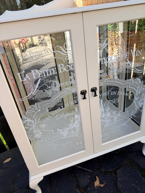 Cabinet with glass doors featuring embossed designs and text. Limestone Cream & White mirrored Display Cabinet with glass shelves