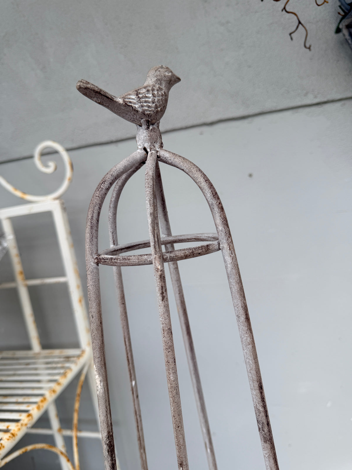 A rustic metal birdcage-style stand with a small bird figurine perched on top