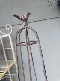 A rustic metal birdcage-style stand with a small bird figurine perched on top