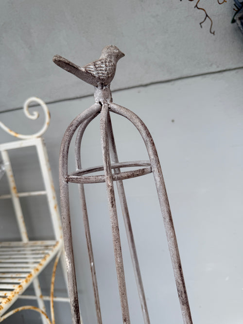 A rustic metal birdcage-style stand with a small bird figurine perched on top