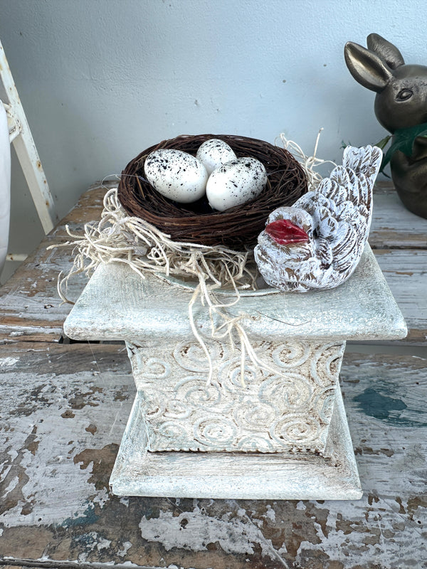 Nest and bird w red beak on rustic plinth white