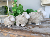 Three small textured sheep figurines in a light beige stone-like finish, arranged from smallest to largest