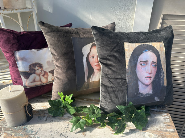Decorative pillows with printed faces on a surface with greenery Velvet Cushion Midnight Mary II The Villa Collection